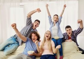 A group of friends of fans watching a sports TV sitting on a sofa in the room.